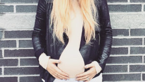 pregnant woman holding her baby bump while standing in front of a brick wall