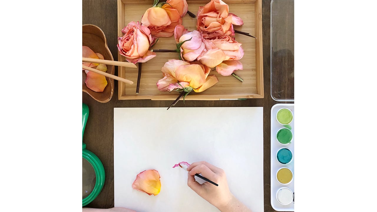a kid painting a picture of rose petals that are in front of them