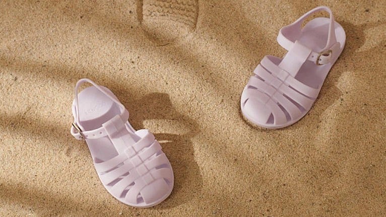 a photo of lavender jelly sandals for kids in the sand