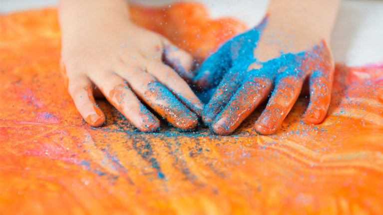 Kid's hands playing with orange paint and blue glitter