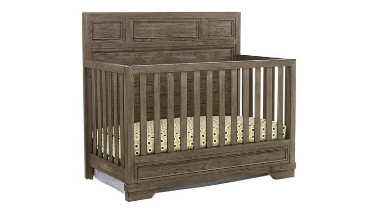 The Westwood Design Foundry Convertible Crib, a brown wooden baby crib with spotted sheets