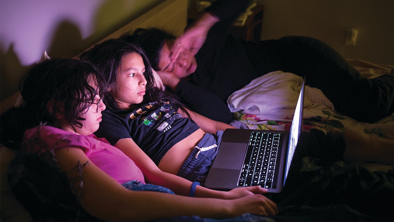 Three family members cuddled together with a laptop watching a movie in the dark