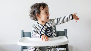 toddler in high chair crying with their arm reaching out