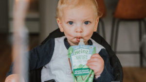 Close-up of baby holding and eating from a Heinz By Nature pouch