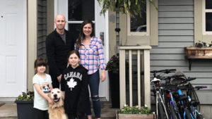 a family of four and their dog standing in front of their home