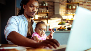 Dad working on laptop while holding baby