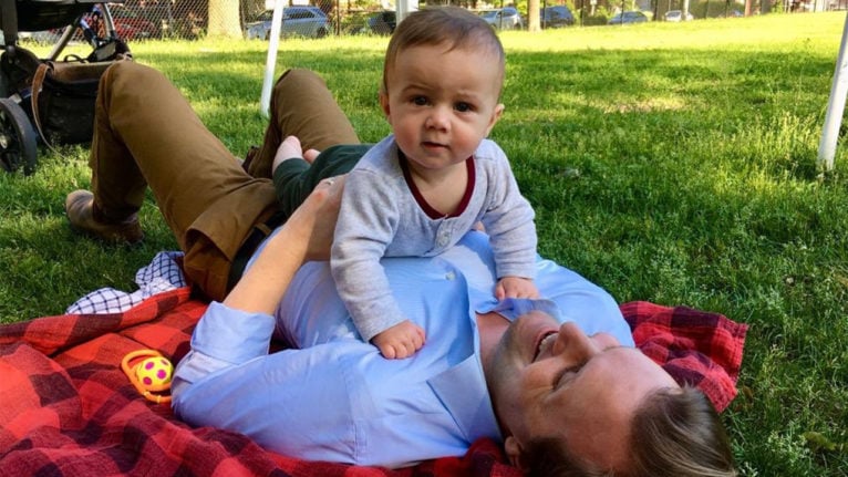 Joe laying down on grass with his son Jude laying on his chest
