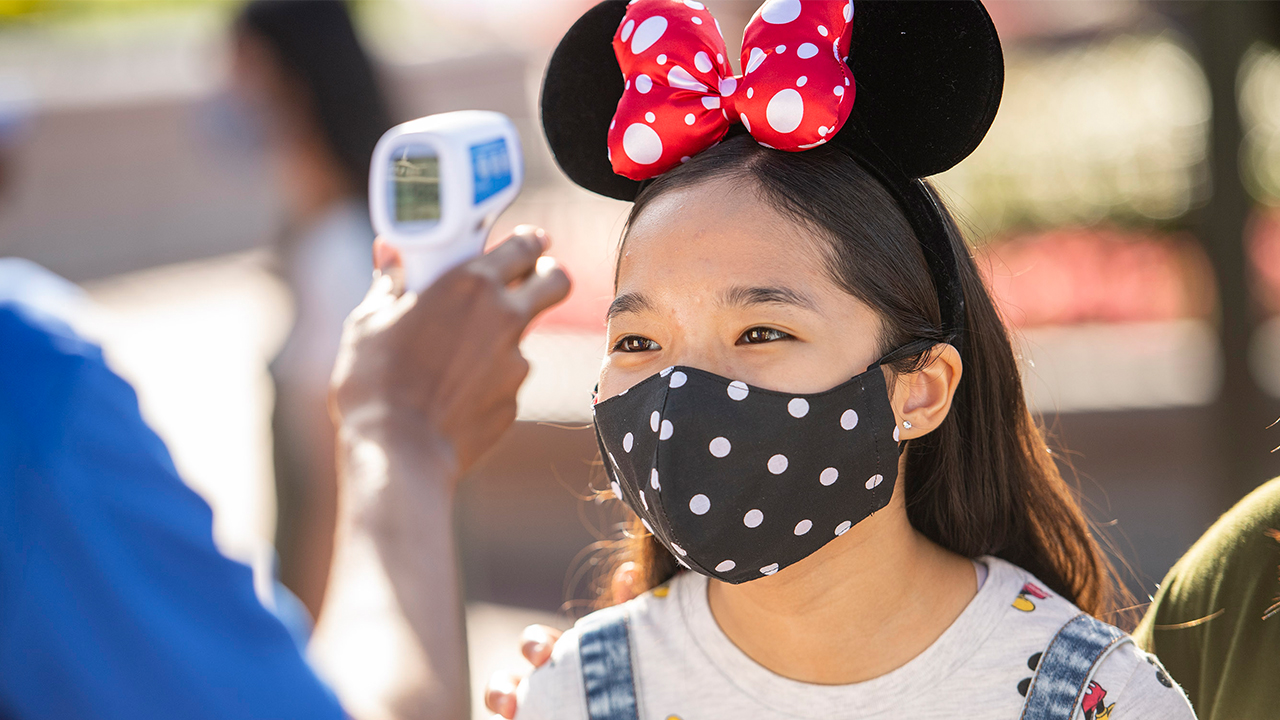 guest wearing minnie mouse ears and a mask getting their temperature checked