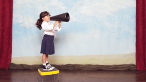 kid standing on a stool on a stage talking into a megaphone