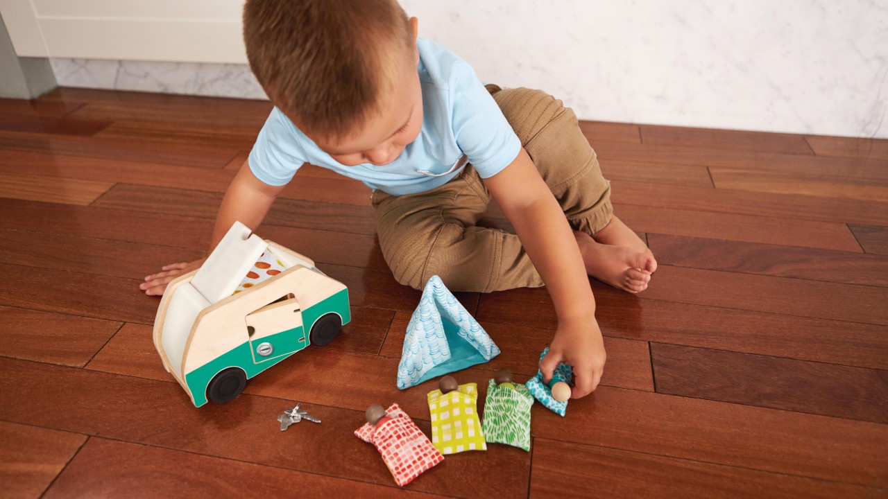 two-year-old playing with wooden toy camper and wooden people in sleeping bags