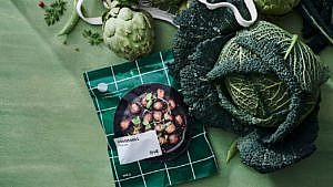 lifestyle shot of packaged meatballs on green background surrounded by vegetables
