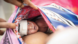 premature baby snuggled against moms chest under a blanket