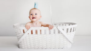 Baby wearing a paper crown, sitting in a white basket