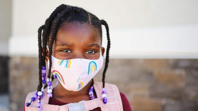 young girl wearing a rainbow mask and backpack