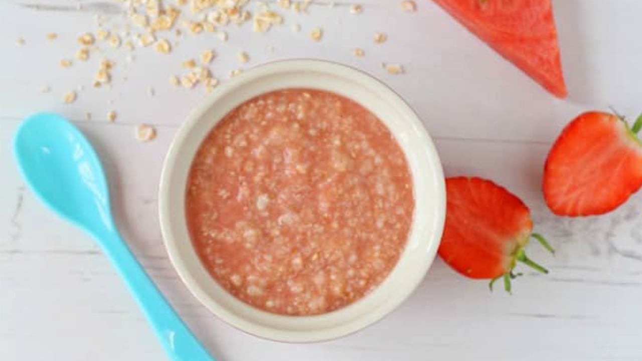 baby food recipes bowl of pink oatmeal with strawberries and watermelon laying next to it