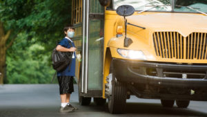 kid wearing a mask getting onto a school bus