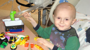 a young child with cancer playing with toys on a hospital bed