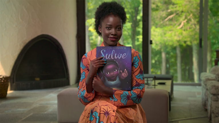 Lupita Nyong'o holding up her childrens book Sulwe to read
