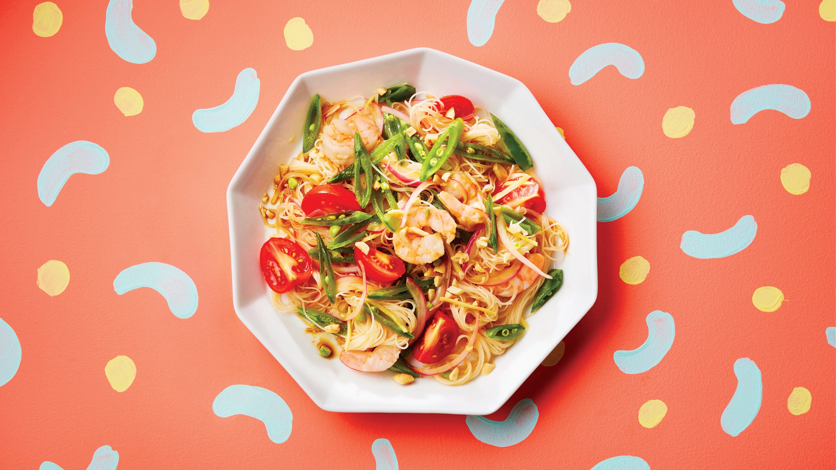A plated dish of shrimp and vegetable noodle salad on a colourful backdrop