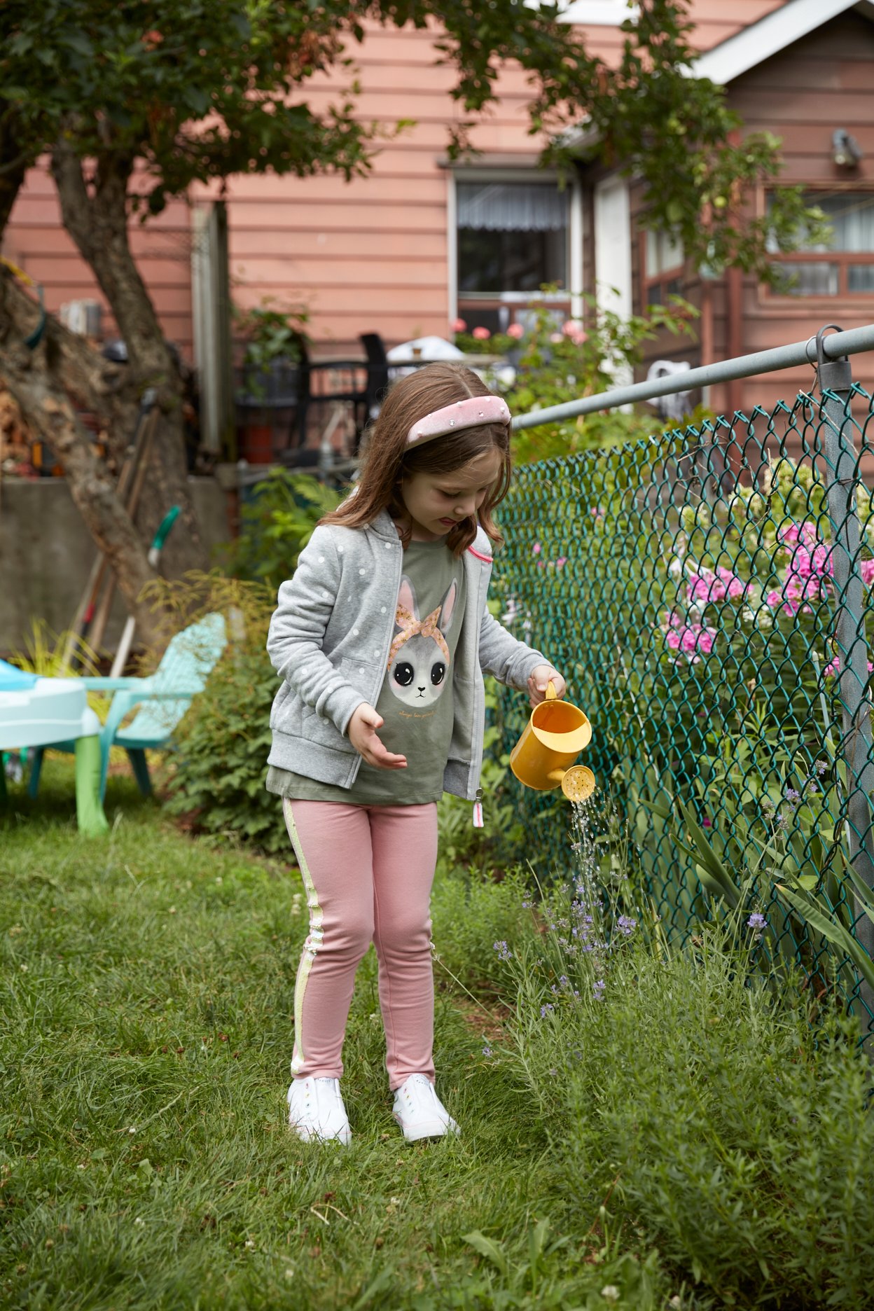 Young girl wearing pink leggings and a hoodie watering plants in backyard