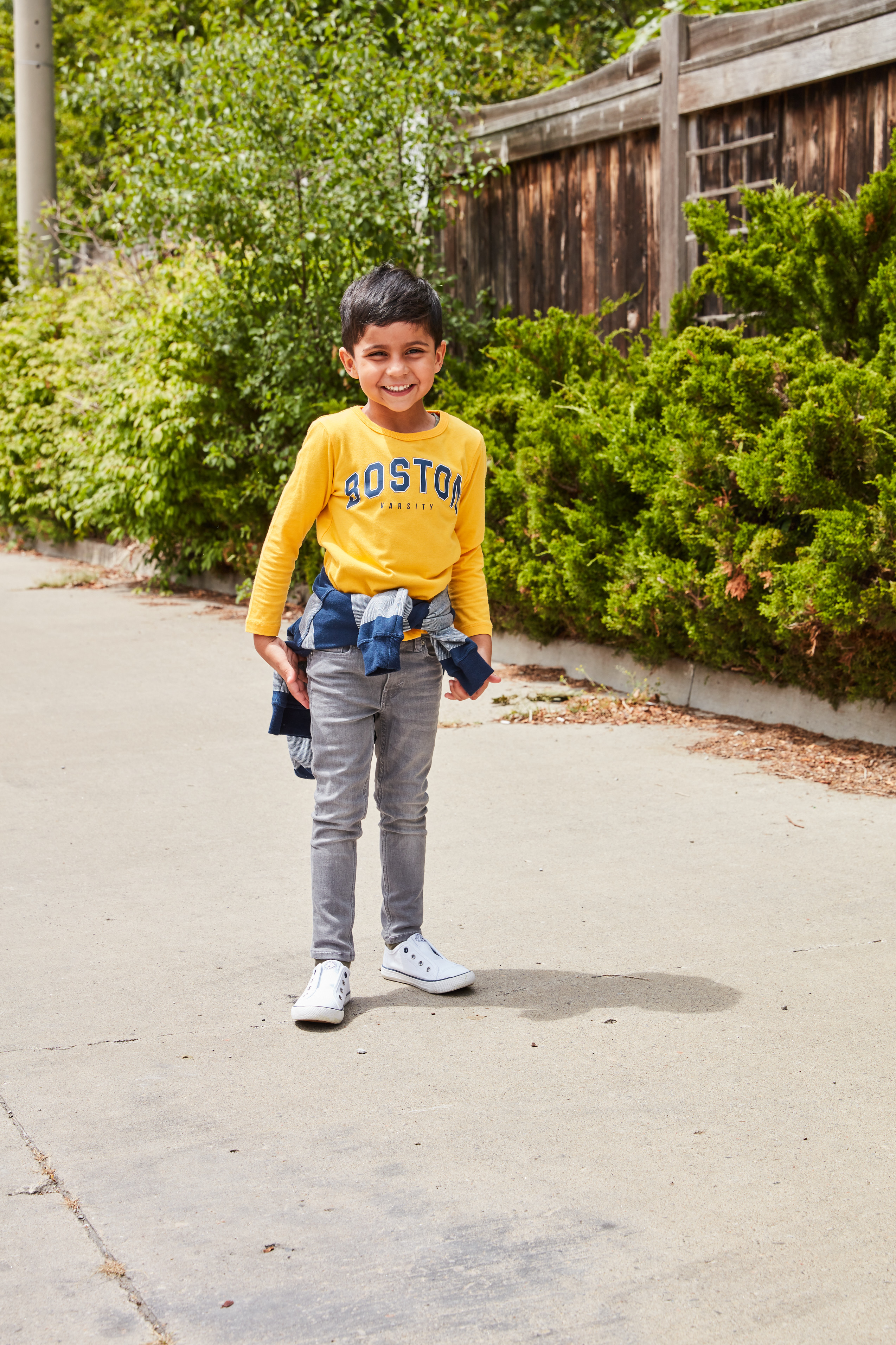 Young boy wearing a "Boston" varsity shirt on sidewalk