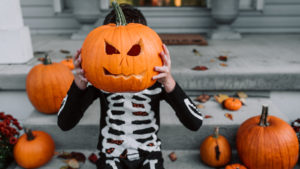 A young boy sitting on the porch with his carved pumpkin at halloween