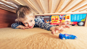 Child reaches under bed to grab toy before any kids organization methods have been put in place