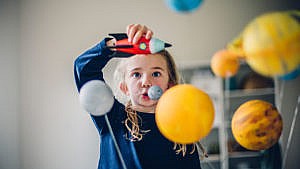 Girl playing with toy rocket ship with planets floating