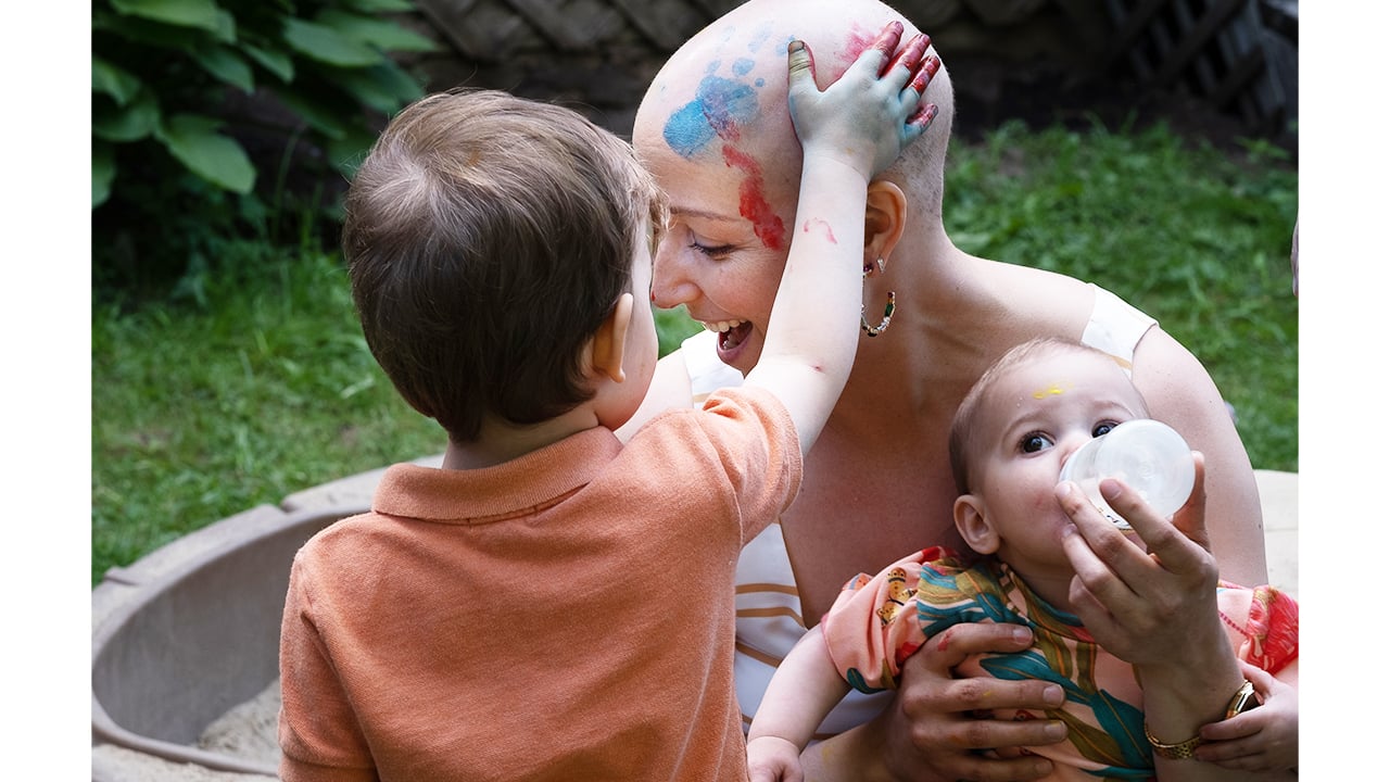 mom cares for baby while older kid finger paints on her bald head