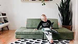 Photo of kid lounging on a kids' couch reading a picture book