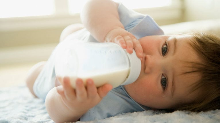 a baby lying down while drinking from a bottle