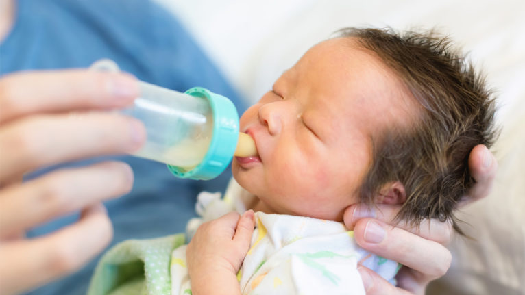 a newborn baby being bottle fed by a nurse