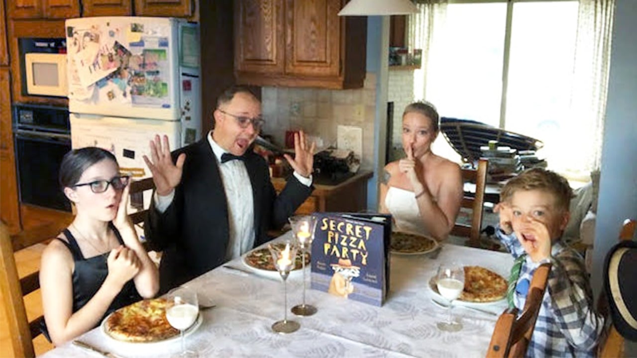 Photo of a family dressed up in fancy clothes at their dining table eating pizza