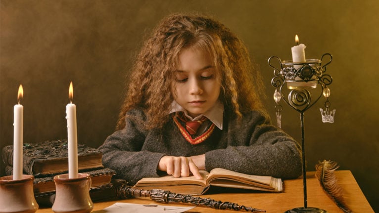 little girl dressed as a student at hogwarts while reading a big book by candlelight