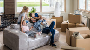 photo of family relaxing on a couch that is wrapped in plastic. Moving boxes are strewn about the room with a view of the backyard visible behind them