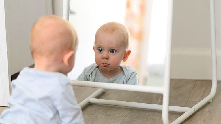 Photo of a baby looking at their reflection in the mirror
