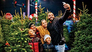 A family with their son, daughter and grandmother taking a selfie among Christmas trees