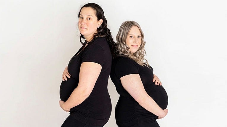 Photo of a lesbian couple with double pregnancies holding their baby bumps
