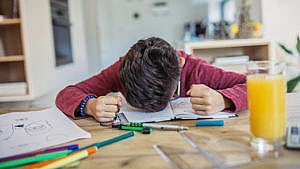 Photo of a kid with their head down in frustration on a notebook and their hands are balled into fists