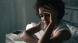 photo of a woman sitting up in bed in the dark with a headache