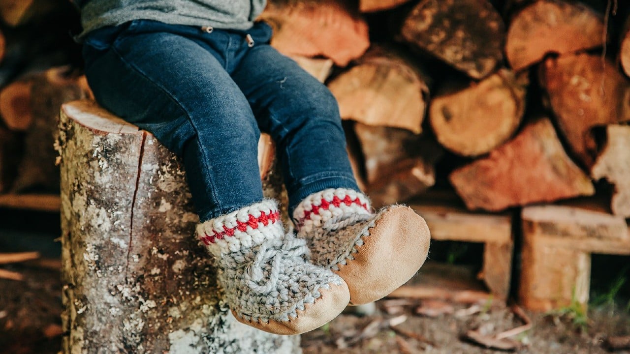 kid sitting on log wearing cozy knit booties