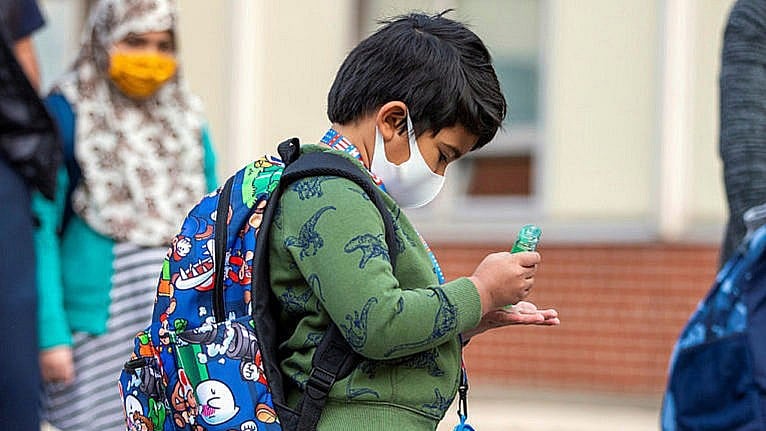 A student uses hand sanitizer as he arrives at school wearing his backpack and mask