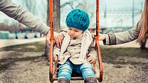 Photo of a child sitting on a swing wearing fall attire while their mom and dad hold each side of the swing making it look like a power struggle