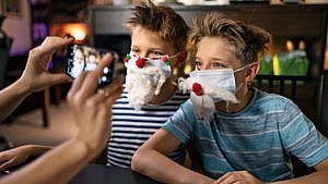 photo of a parent taking a picture of two kids wearing facemasks that have been decorated to look like santa's beard