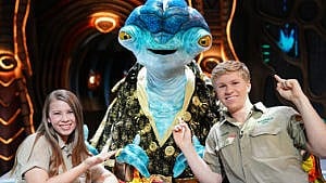 A still from the Disney+ show Earth to Ned showing a big blue alien posing for a picture with Steve Irwin's kids Bindi and Robert