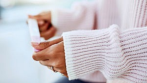 A woman's arms in a pink ribbed sweater holding a pregnancy test
