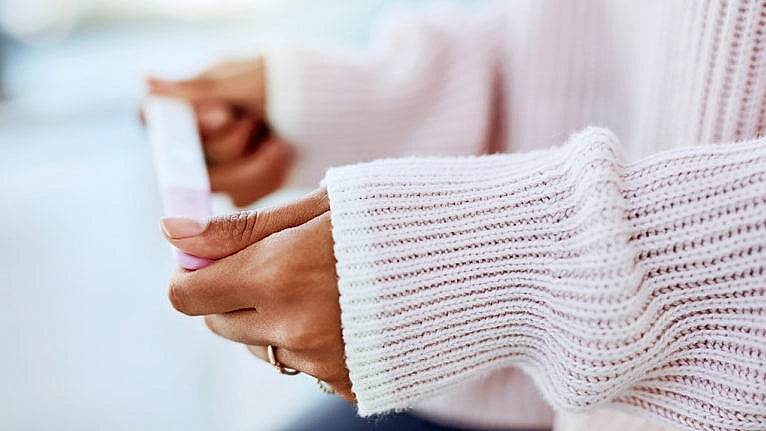 A woman's arms in a pink ribbed sweater holding a pregnancy test