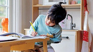 Photo of a kid sitting at a table practicing writing in a notebook