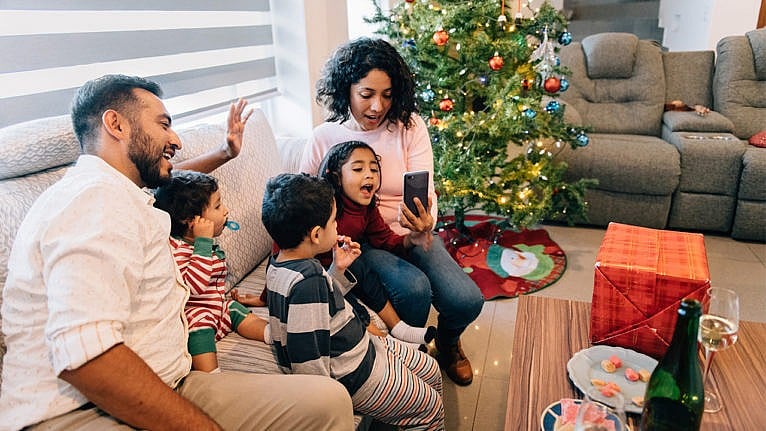 Photo of a family with young kids sitting on their couch video chatting with family during the holidays