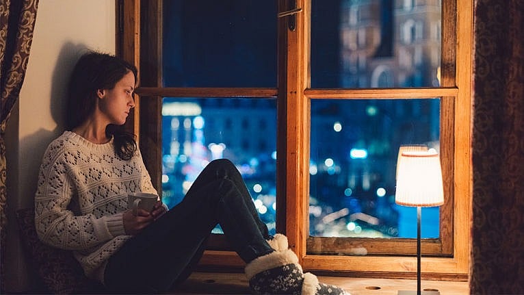 Photo of a woman sitting thoughtfully in front of a window at night dressed in wintery clothes.